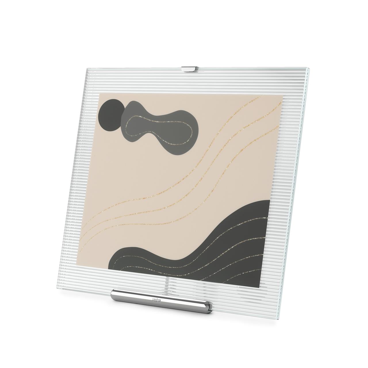 Der FLUTE Bilderrahmen 20x25 in Chrom zeigt ein modernes, geriffeltes Glasdesign mit einem schlichten, eleganten Standfuß. Im Rahmen befindet sich ein abstraktes Bild mit schwarzen und goldenen Linien auf beigem Hintergrund.