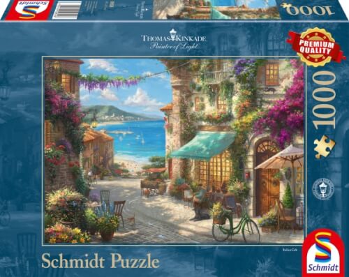 Das Bild zeigt die Verpackung eines Schmidt Puzzles mit 1000 Teilen, das ein malerisches Küstendorf mit bunten Häusern und Blick aufs Meer darstellt. Auf der Verpackung steht auch der Name des Künstlers Thomas Kinkade.