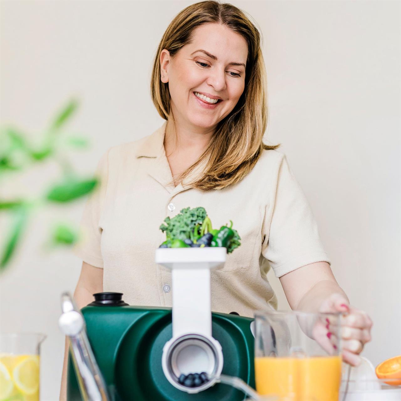 Eine Frau benutzt das Produkt "Go Green Package", um frischen Saft zuzubereiten. Vor ihr stehen frisches Gemüse und ein Glas mit Orangensaft.