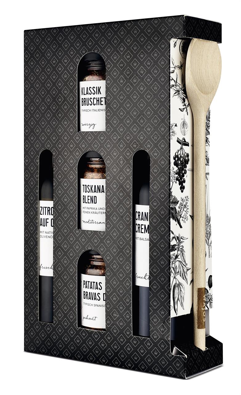 Das Bild zeigt ein Geschenkset mit verschiedenen Gewürzen und Ölen sowie einem Holzlöffel. Die Verpackung ist elegant gestaltet und die Produkte sind schön angeordnet.