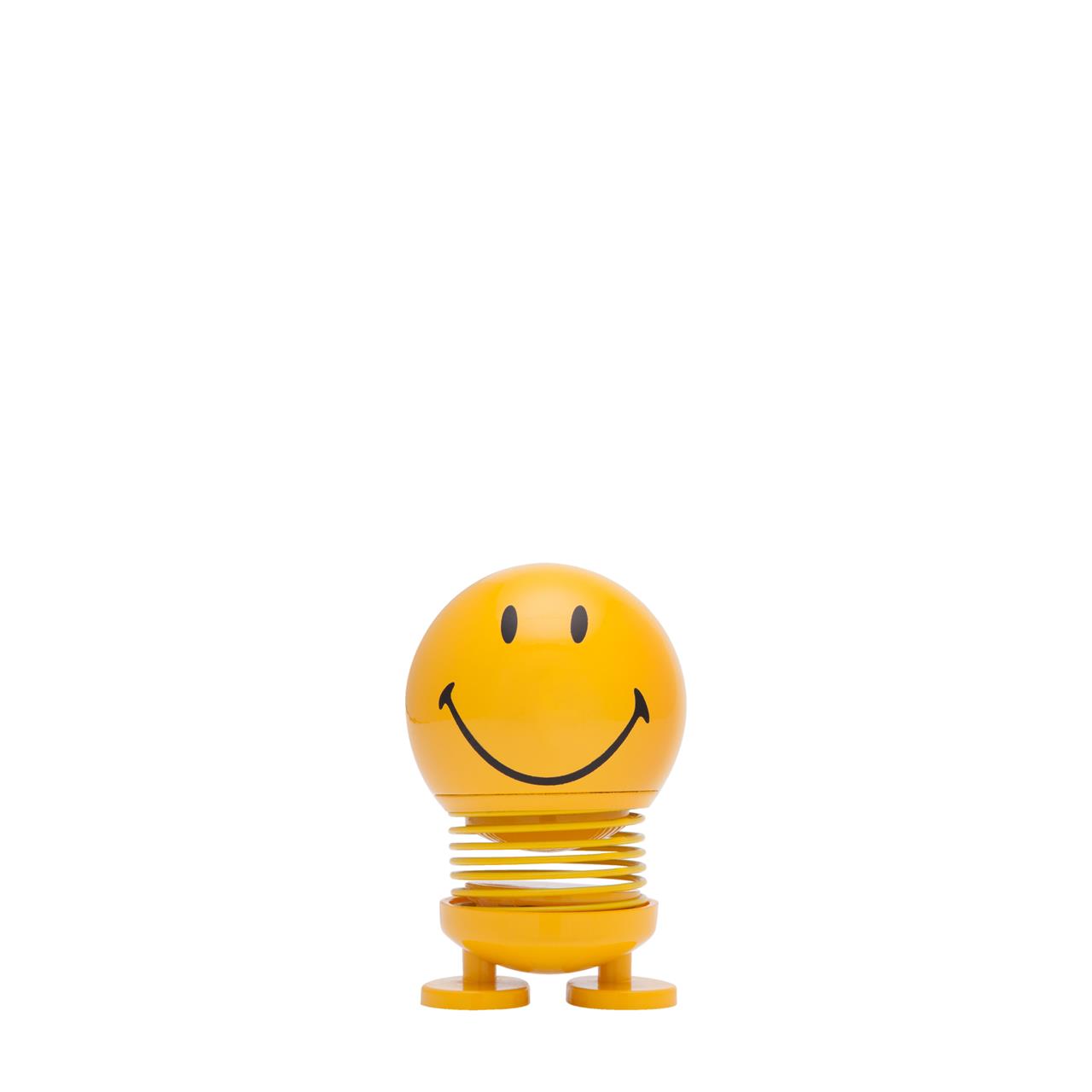 Das Bild zeigt einen gelben Hoptimist mit einem großen Smiley-Gesicht. Die Figur steht auf zwei kleinen Füßen und hat eine Feder in der Mitte.