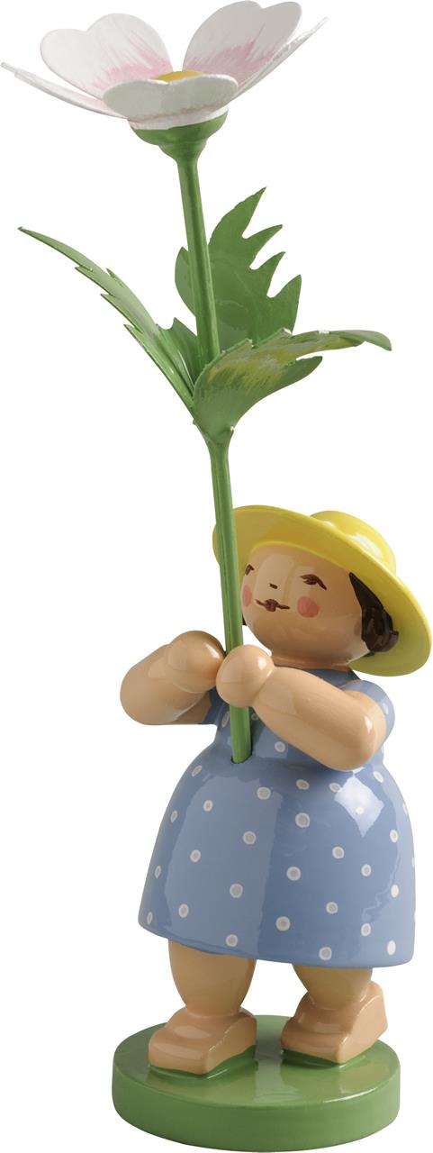 Das Bild zeigt eine kleine Holzfigur eines Mädchens in einem blauen gepunkteten Kleid. Sie hält eine große Buschwindrose in den Händen und trägt einen gelben Hut.