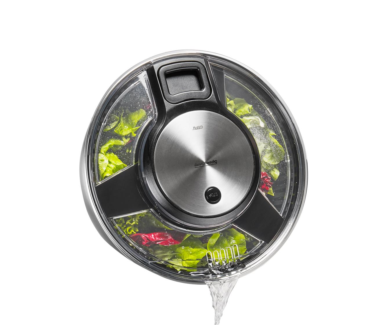 Die Abbildung zeigt eine Salatschleuder SPEEDWING® aus Edelstahl, gefüllt mit frischem Salat. Durch die transparente Schüssel wird gerade Wasser abgegossen.