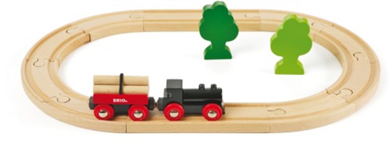 Das Bild zeigt das BRIO® Bahn Starterset 33042 mit einer kleinen Holzeisenbahn auf ovaler Strecke. Im Set sind zudem zwei grüne Bäume und ein Waggon mit Holzladung enthalten.