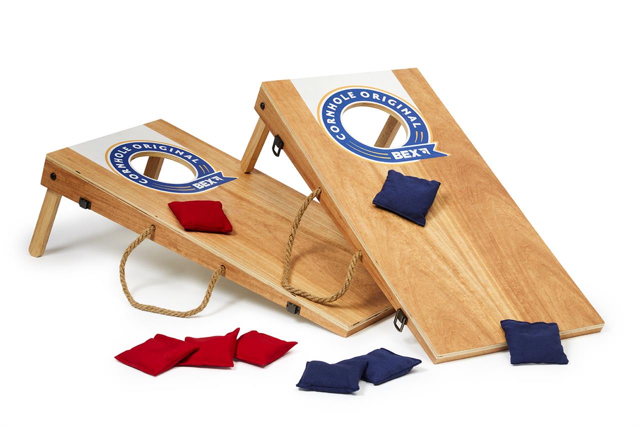 Das Bild zeigt das Spiel "Cornhole Original" mit den Maßen 60,5 x 30,7 cm. Zwei Holzbretter mit jeweils einem Loch und mehrere rote und blaue Wurfsäckchen sind darauf zu sehen.