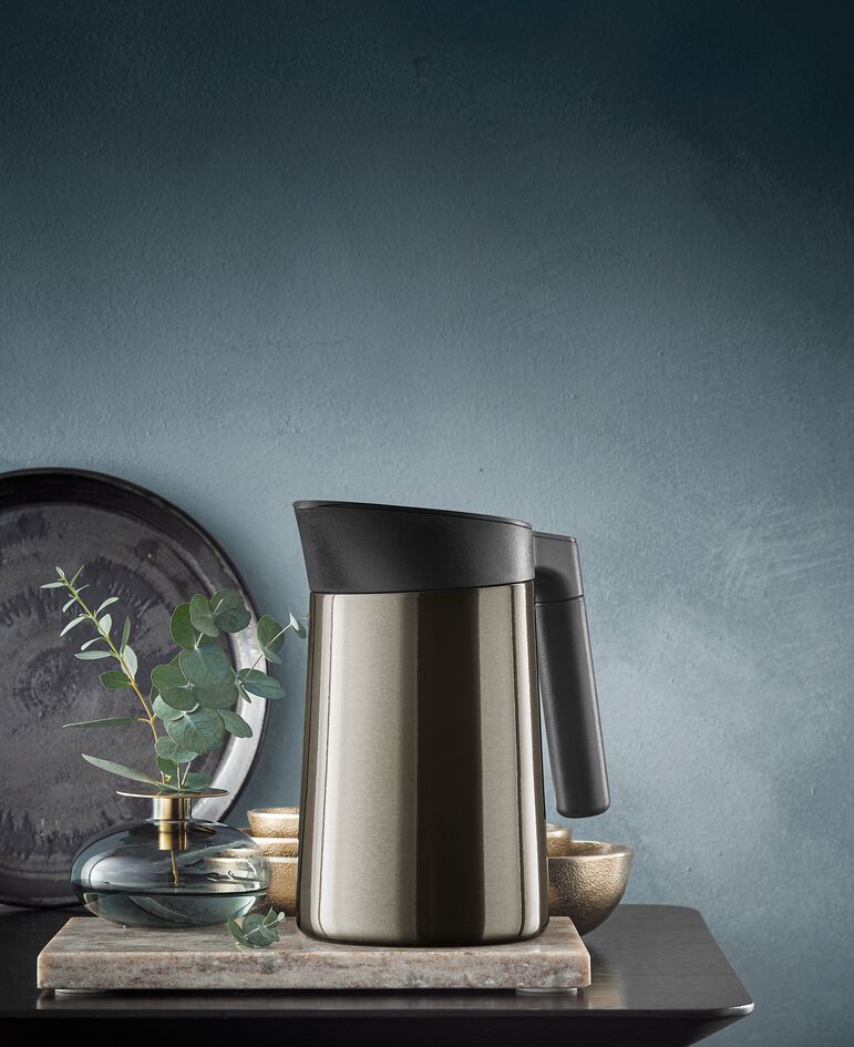 Die Abbildung zeigt die Isolierkanne Grafi 1,0 l Kineo. Die Kanne steht auf einem Tisch neben einer kleinen Vase mit Eukalyptuszweigen.