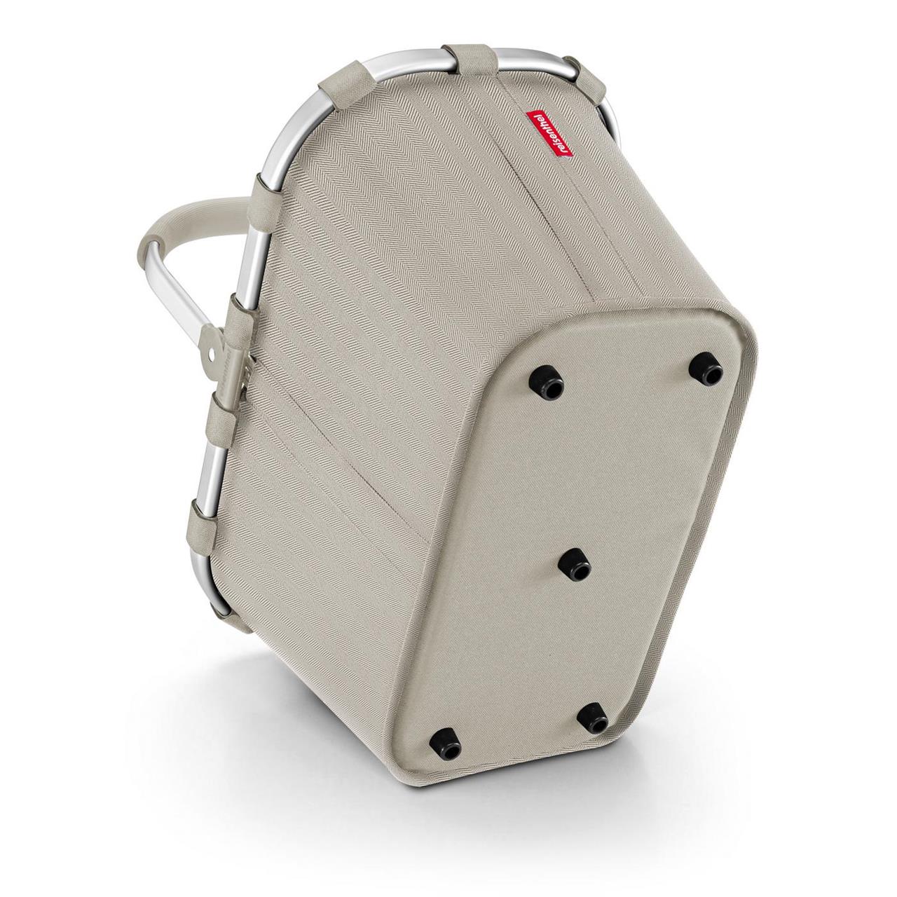 Das Bild zeigt den Einkaufskorb "Carrybag Herringbone Sand" in sandfarbener Optik. Der Korb hat einen stabilen Aluminiumrahmen und steht auf vier kleinen Füßen.