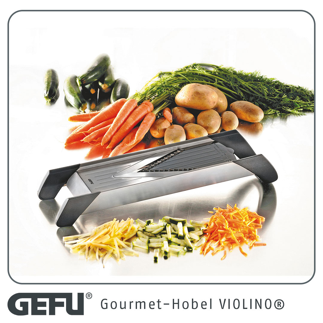 Das Bild zeigt den Gourmet-Hobel Violino zusammen mit frischem Gemüse wie Karotten, Kartoffeln und Zucchini. Vor dem Hobel liegen bereits in Streifen geschnittene Gemüsestücke.