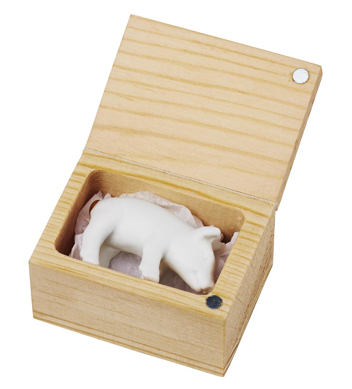 Das Bild zeigt ein kleines Glücksschwein aus weißem Material, das in einer offenen Holzkiste liegt. Das Schwein ist auf etwas Papier gebettet und die Schachtel hat einen Deckel mit Magnetverschluss.