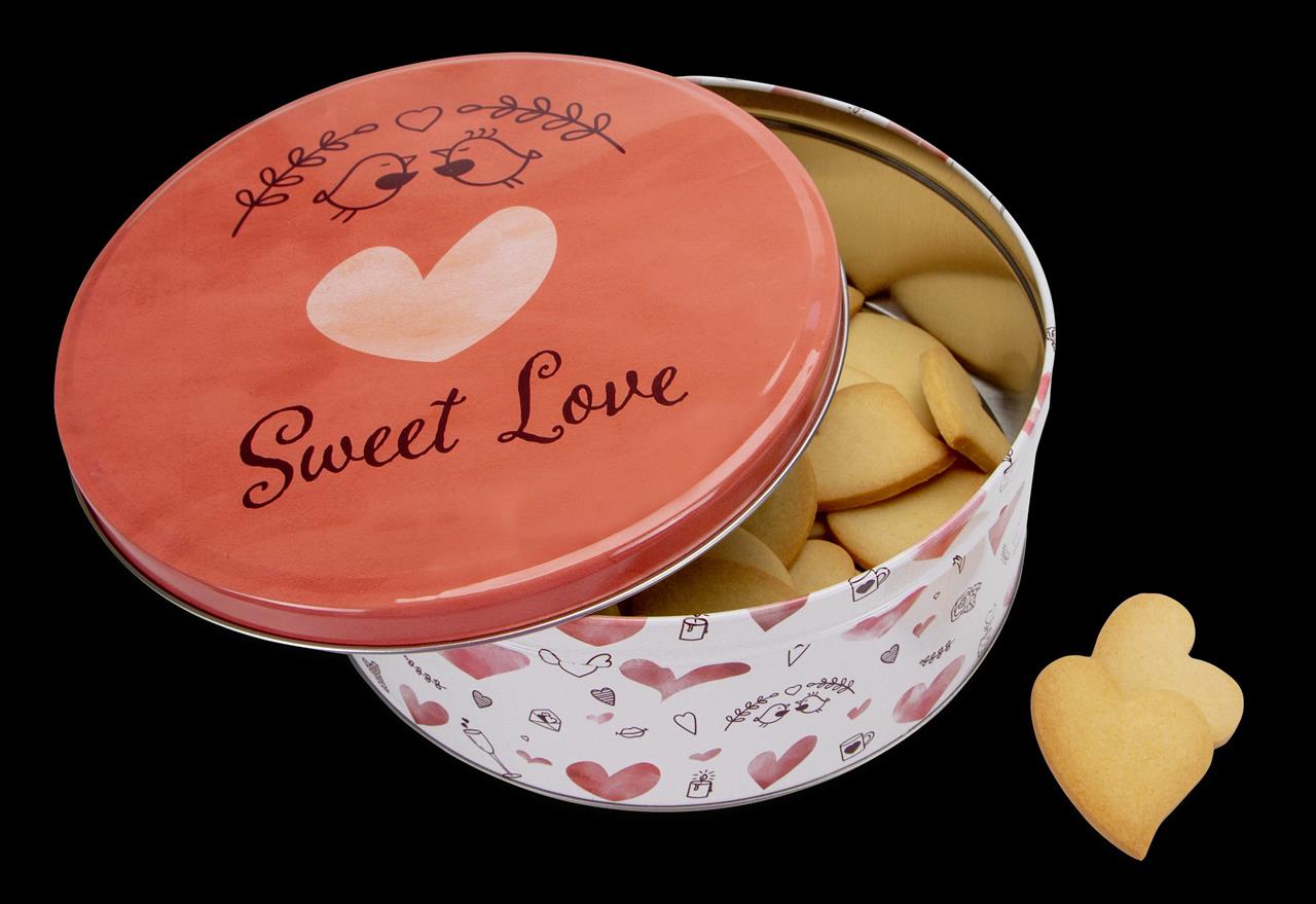 Die Abbildung zeigt eine runde Gebäckdose mit dem Schriftzug "Sweet Love" und herzförmigen Dekorationen. In der Dose befinden sich Kekse, und davor liegen zwei herzförmige Kekse.