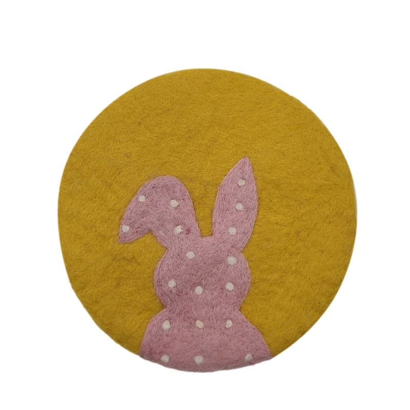 Auf dem Bild ist ein runder Untersetzer in goldgelber Farbe zu sehen. Darauf ist ein rosa Hase mit weißen Tupfen abgebildet.