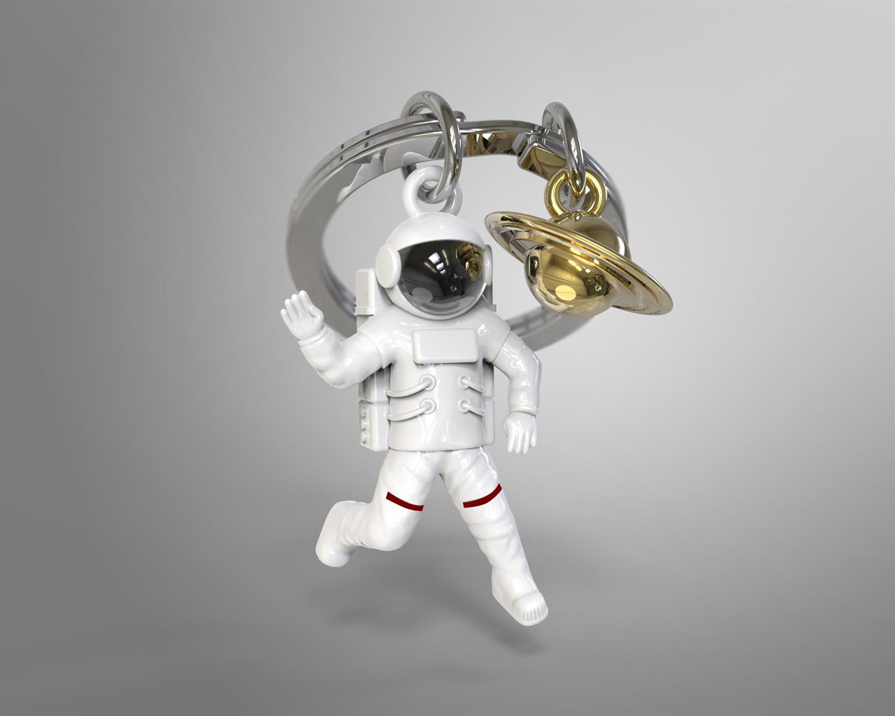 Auf dem Bild ist ein Schlüsselanhänger mit einem Astronauten im weißen Anzug zu sehen. Daneben hängt ein goldener Saturn als Anhänger am Schlüsselring.
