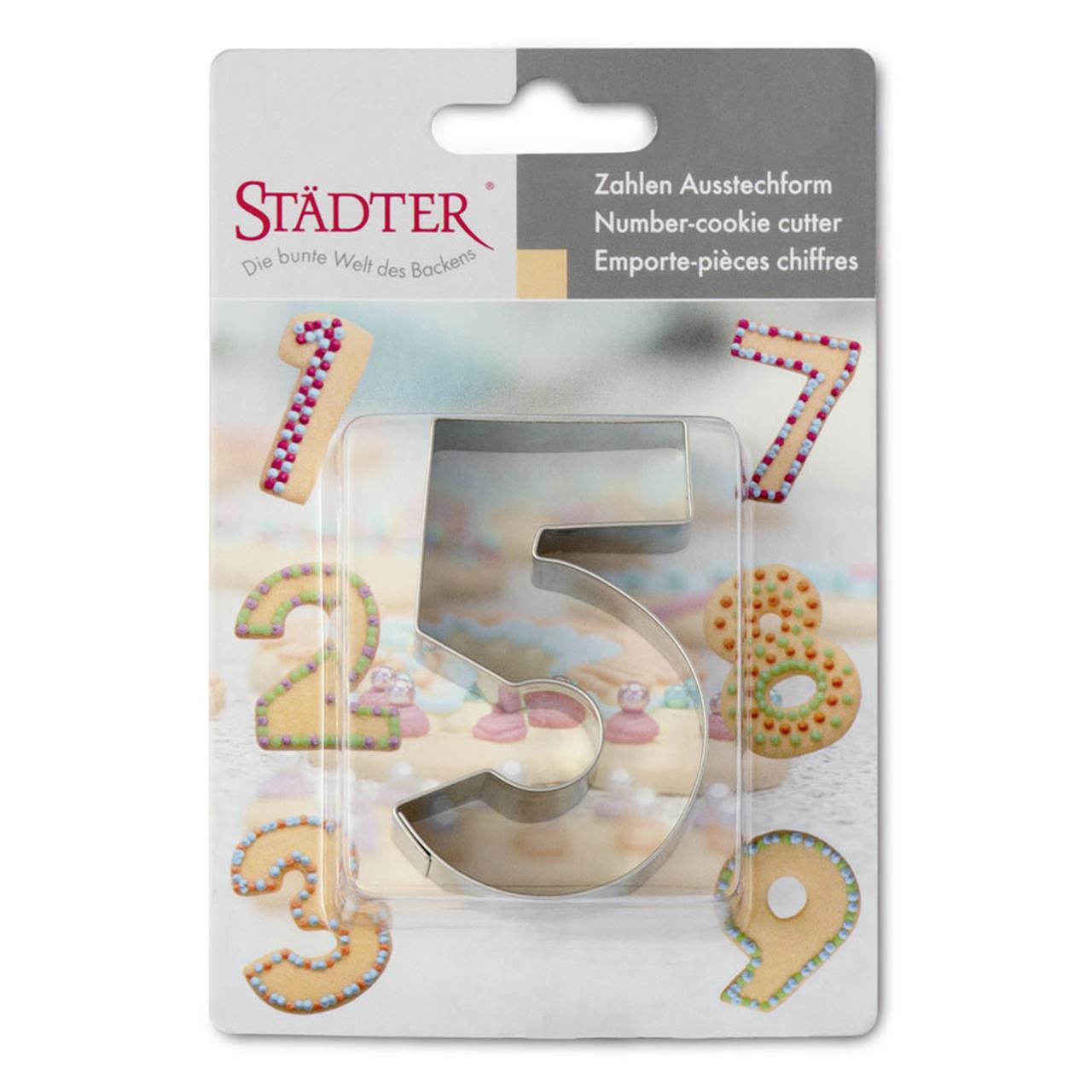 Auf dem Bild ist ein Zahlenausstecher in Form der Zahl 5 aus Edelstahl zu sehen. Die Verpackung zeigt dekorierte Kekse in Zahlenform rund um den Ausstecher.