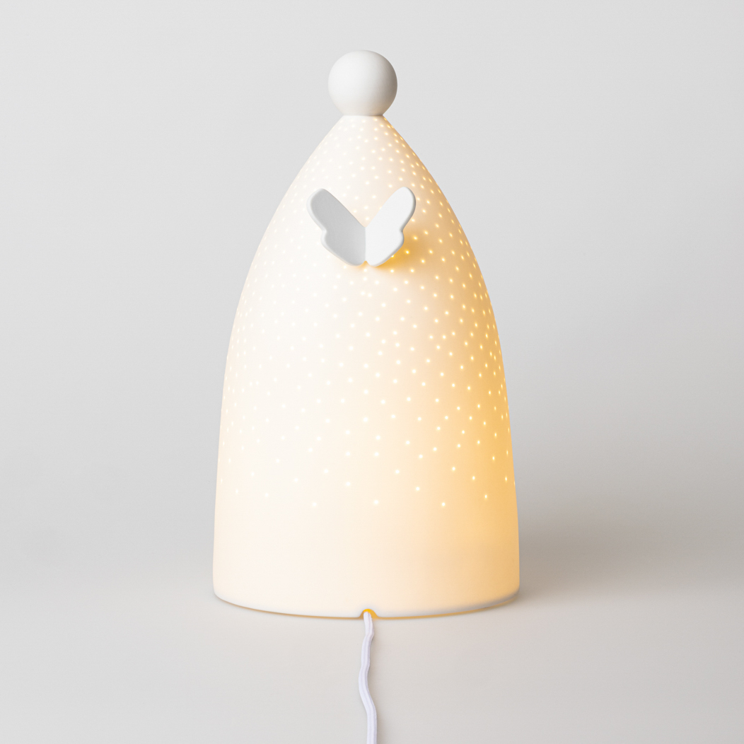 Auf dem Bild ist eine dekorative Lampe in Form einer Figur mit einem Schmetterlingsausschnitt zu sehen. Die Lampe leuchtet warm und hat viele kleine Lichtpunkte auf ihrer Oberfläche.
