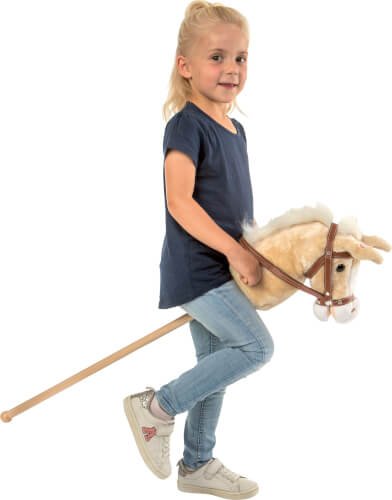 Ein kleines Mädchen reitet auf einem Steckenpferd. Sie trägt ein dunkelblaues T-Shirt und eine hellblaue Jeans.
